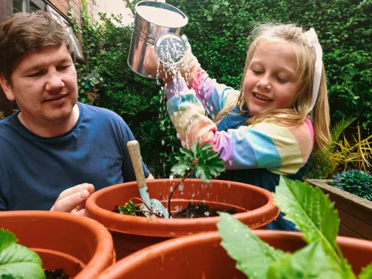 Vater und Tochter gießen gemeinsam Pflanzen in Terrakottatöpfen