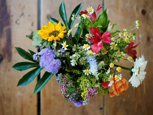 Bunter Sommerstrauß mit Sonnenblume, Kamille und Rosen vor einer Holzwand